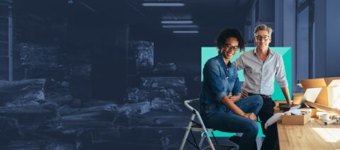 Two people sitting in a warehouse.|Business people looking at a computer screen.|