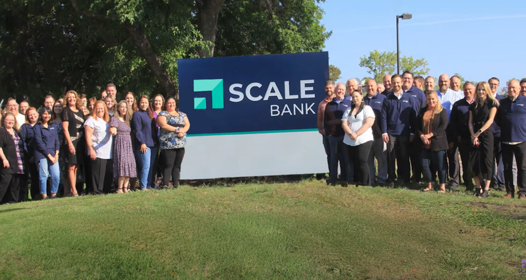 Scale Bank staff photo in front of sign,