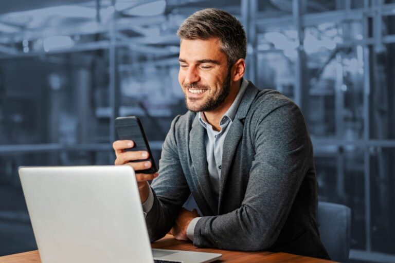 Man looking at his phone in front of a laptop